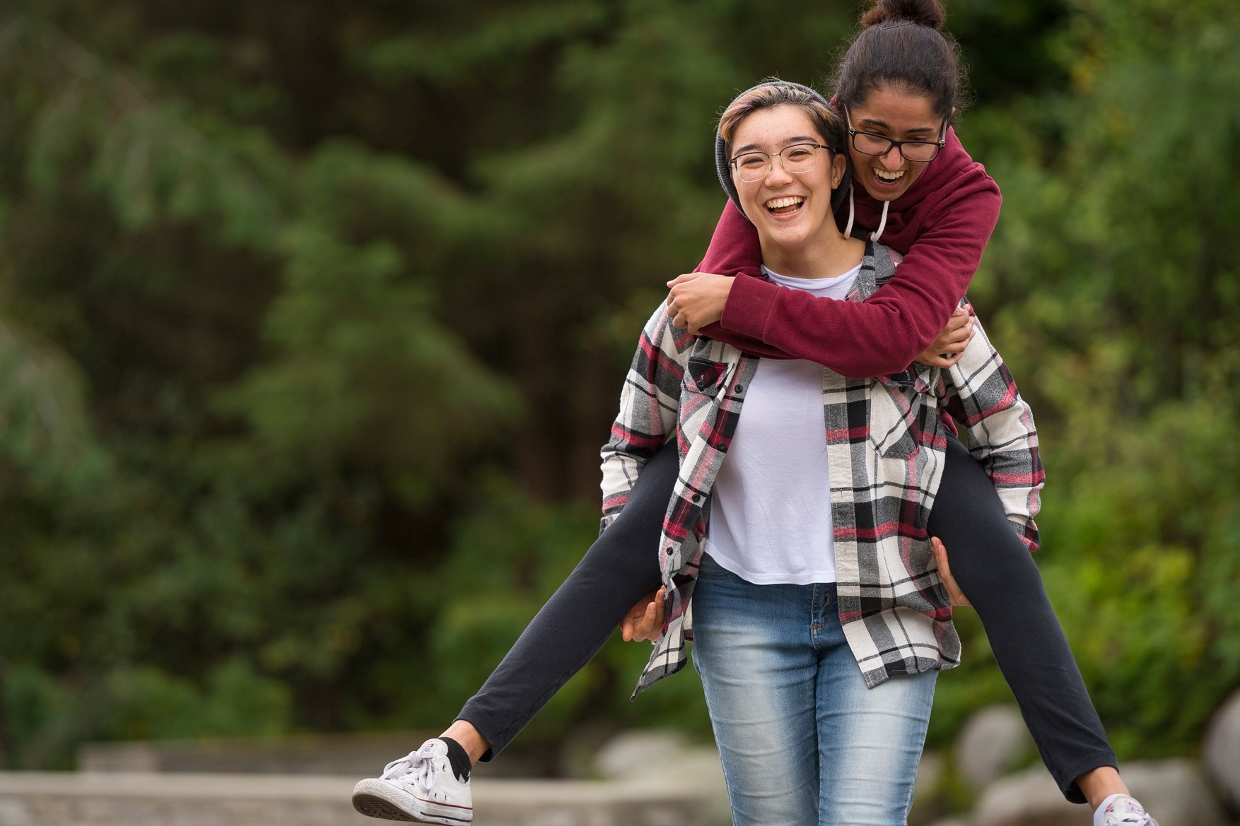 A student piggybacks another student on SFU campus, both are smiling and having a good time